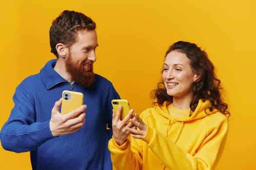 Man and woman couple smiling merrily with phone in hand social media viewing photos and videos, on yellow background, symbols signs and hand gestures, family freelancers. High quality photo