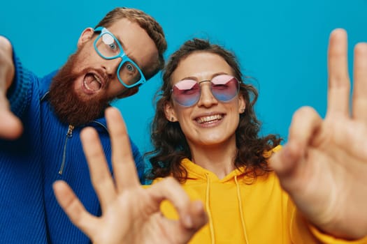 A woman and a man fun couple cranking and showing signs with their hands smiling cheerfully, on a blue background, The concept of a real relationship in a family. High quality photo