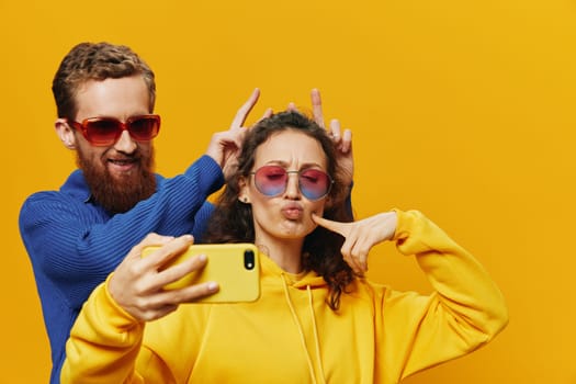 Woman and man funny couple with phones in hand social networking and communication crooked do selfies smile fun, on yellow background. The concept of real family relationships, freelancers, work online. High quality photo