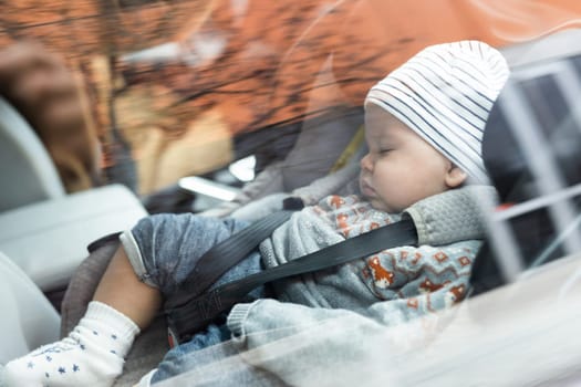 Cute little baby boy sleeping strapped into infant car seat in passenger compartment during car drive