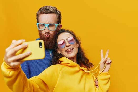 Woman and man funny couple with phones in hand social networking and communication crooked do selfies smile fun, on yellow background. The concept of real family relationships, freelancers, work online. High quality photo