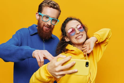 Woman and man funny couple with phones in hand social networking and communication crooked do selfies smile fun, on yellow background. The concept of real family relationships, freelancers, work online. High quality photo