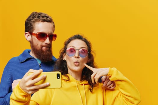 Woman and man funny couple with phones in hand social networking and communication crooked do selfies smile fun, on yellow background. The concept of real family relationships, freelancers, work online. High quality photo