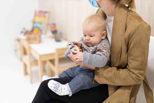 Mother holding infant baby boy in her lap, sitting and waiting in front of doctor's office for pediatric well check. child's health care concept.