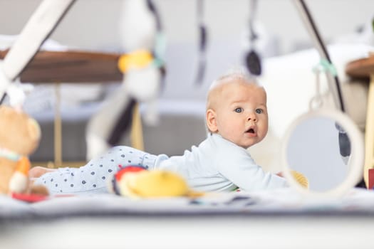 Cute baby boy playing with hanging toys arch on mat at home Baby activity and play center for early infant development. Baby playing at home.