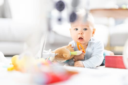 Cute baby boy playing with hanging toys arch on mat at home Baby activity and play center for early infant development. Baby playing at home.