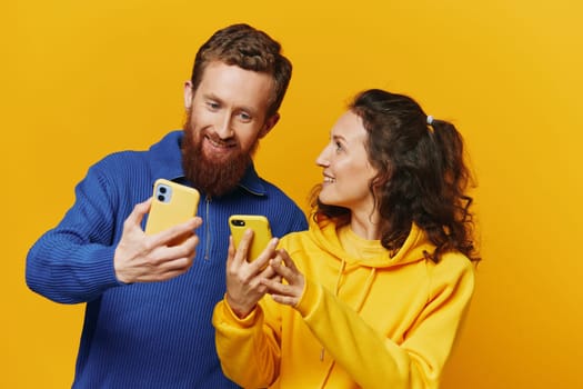 Man and woman couple smiling merrily with phone in hand social media viewing photos and videos, on yellow background, symbols signs and hand gestures, family freelancers. High quality photo