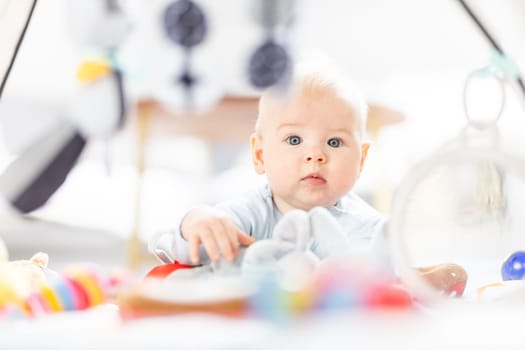 Cute baby boy playing with hanging toys arch on mat at home Baby activity and play center for early infant development. Baby playing at home.