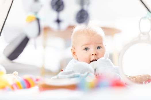 Cute baby boy playing with hanging toys arch on mat at home Baby activity and play center for early infant development. Baby playing at home.