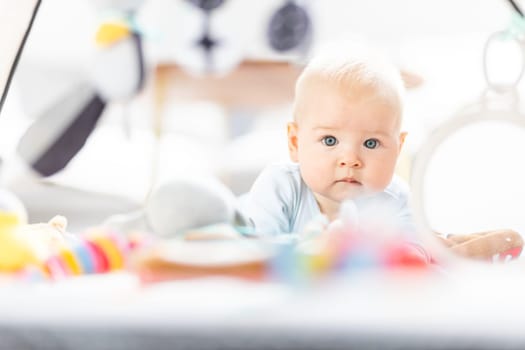 Cute baby boy playing with hanging toys arch on mat at home Baby activity and play center for early infant development. Baby playing at home.