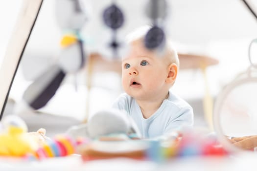 Cute baby boy playing with hanging toys arch on mat at home Baby activity and play center for early infant development. Baby playing at home.