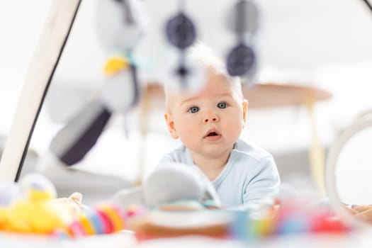 Cute baby boy playing with hanging toys arch on mat at home Baby activity and play center for early infant development. Baby playing at home.