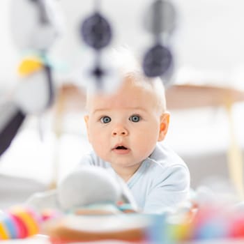 Cute baby boy playing with hanging toys arch on mat at home Baby activity and play center for early infant development. Baby playing at home.