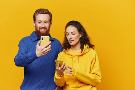 Man and woman couple smiling merrily with phone in hand social media viewing photos and videos, on yellow background, symbols signs and hand gestures, family freelancers. High quality photo