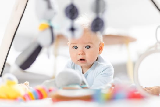 Cute baby boy playing with hanging toys arch on mat at home Baby activity and play center for early infant development. Baby playing at home.