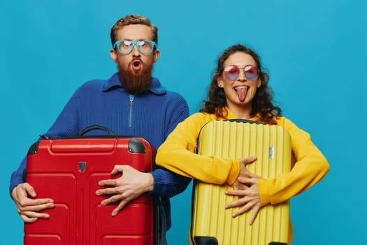 Woman and man smile suitcases in hand with yellow and red suitcase smile fun, on blue background, packing for a trip, family vacation trip. High quality photo