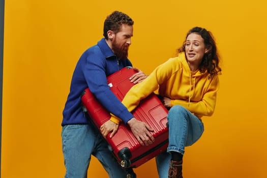 Woman and man smiling, suitcases in hand with yellow and red suitcase smiling merrily and crooked, yellow background, going on a trip, family vacation trip, newlyweds. High quality photo