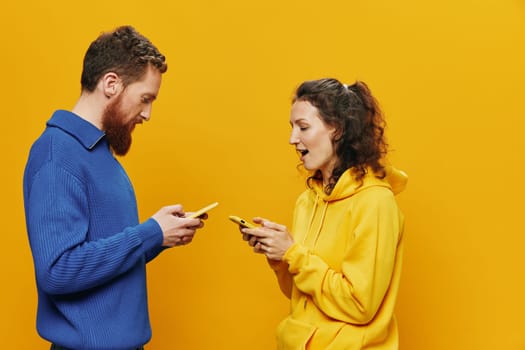 Woman and man cheerful couple with phones in hand social networking and communication crooked smile fun and fight, in yellow background. The concept of real family relationships, freelancers, work online. High quality photo