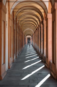 Elegant arches silhouette architectural landmarks in Bologna with happy tourists walking on a sunny warm summer day. The concept of historical heritage. Copyspace.