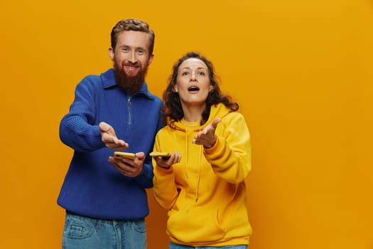 Woman and man cheerful couple with phones in hand social networking and communication crooked smile fun and fight, in yellow background. The concept of real family relationships, freelancers, work online. High quality photo