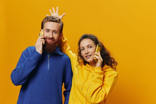 Woman and man cheerful couple with phones in hand talking on cell phone crooked smile cheerful, on yellow background. The concept of real family relationships, talking on the phone, work online. High quality photo