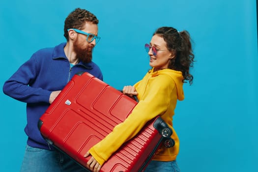 Woman and man smile suitcases in hand with yellow and red suitcase smile fun, on blue background, packing for a trip, family vacation trip. High quality photo