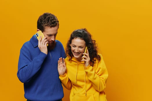 Woman and man cheerful couple with phones in hand talking on cell phone crooked smile cheerful, on yellow background. The concept of real family relationships, talking on the phone, work online. High quality photo