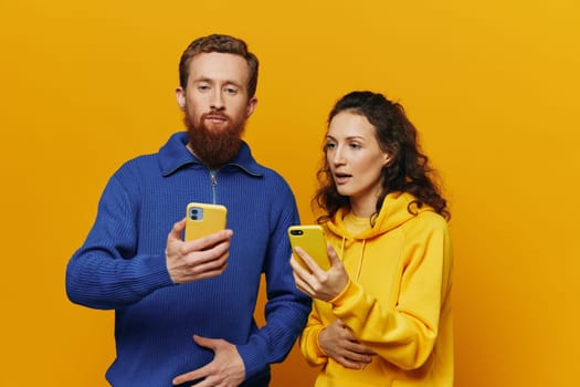 Man and woman couple smiling merrily with phone in hand social media viewing photos and videos, on yellow background, symbols signs and hand gestures, family freelancers. High quality photo