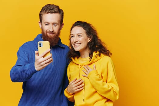 Man and woman couple smiling merrily with phone in hand social media viewing photos and videos, on yellow background, symbols signs and hand gestures, family freelancers. High quality photo