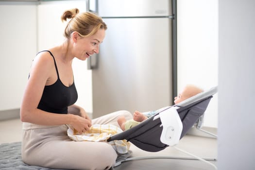 Happy smiling mother playing with her little baby son sitting in electric rocking chair at home. Child development and happy parenting