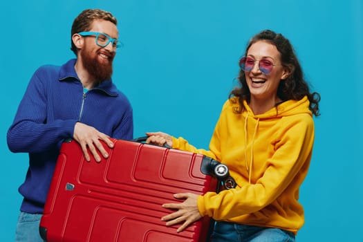 Woman and man smile suitcases in hand with yellow and red suitcase smile fun, on blue background, packing for a trip, family vacation trip. High quality photo