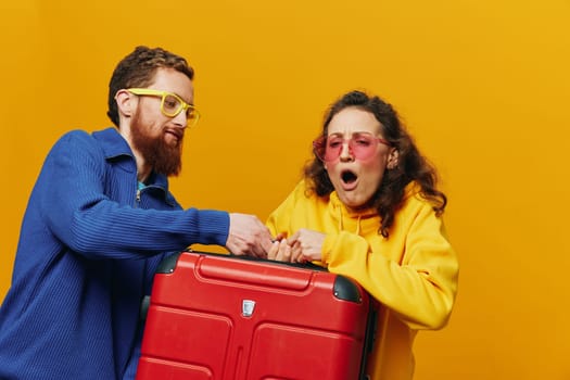 Woman and man smiling, suitcases in hand with yellow and red suitcase smiling merrily and crooked, yellow background, going on a trip, family vacation trip, newlyweds. High quality photo