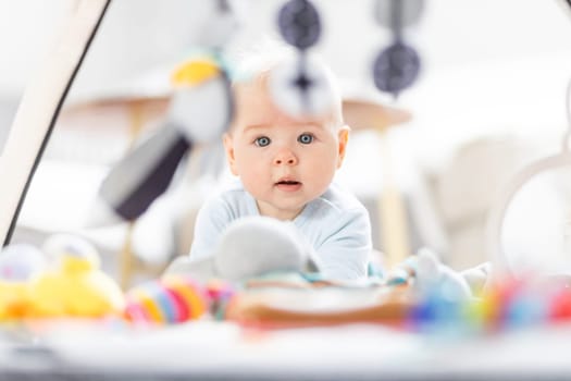 Cute baby boy playing with hanging toys arch on mat at home Baby activity and play center for early infant development. Baby playing at home.