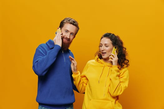 Woman and man cheerful couple with phones in hand talking on cell phone crooked smile cheerful, on yellow background. The concept of real family relationships, talking on the phone, work online. High quality photo