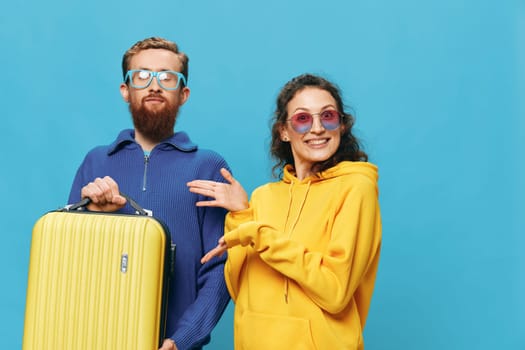 Woman and man smile sitting on suitcase with yellow suitcase smile, on blue background, packing for trip, family vacation trip. High quality photo