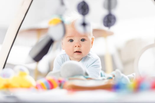 Cute baby boy playing with hanging toys arch on mat at home Baby activity and play center for early infant development. Baby playing at home.