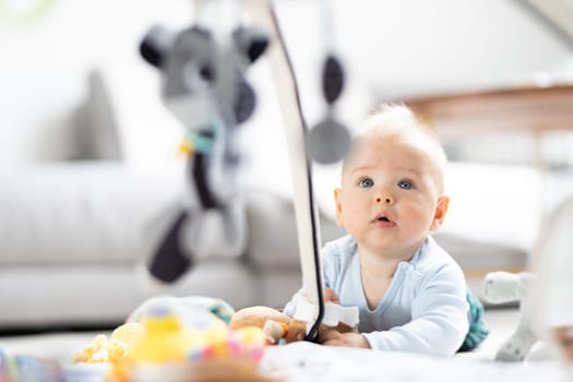 Cute baby boy playing with hanging toys arch on mat at home Baby activity and play center for early infant development. Baby playing at home.