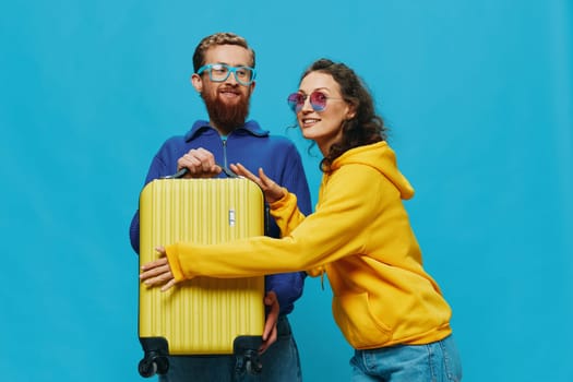 Woman and man smile sitting on suitcase with yellow suitcase smile, on blue background, packing for trip, family vacation trip. High quality photo