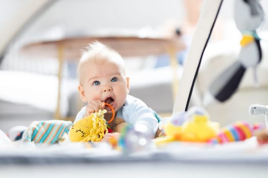 Cute baby boy playing with hanging toys arch on mat at home Baby activity and play center for early infant development. Baby playing at home.