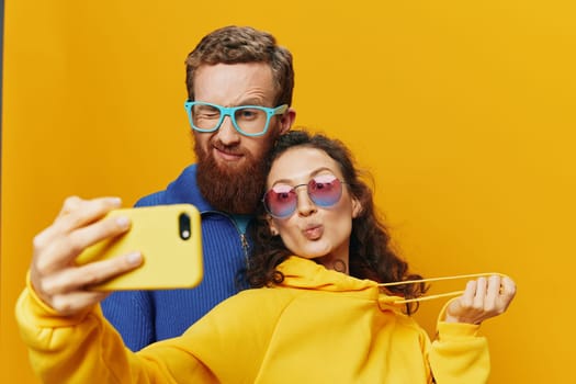 Woman and man funny couple with phones in hand social networking and communication crooked do selfies smile fun, on yellow background. The concept of real family relationships, freelancers, work online. High quality photo