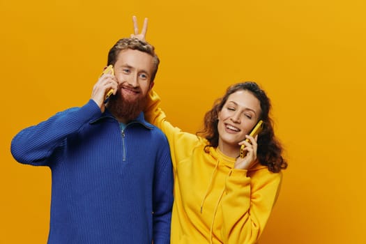 Woman and man cheerful couple with phones in hand talking on cell phone crooked smile cheerful, on yellow background. The concept of real family relationships, talking on the phone, work online. High quality photo