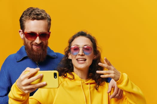 Woman and man funny couple with phones in hand social networking and communication crooked do selfies smile fun, on yellow background. The concept of real family relationships, freelancers, work online. High quality photo