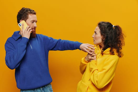 Woman and man cheerful couple with phones in hand social networking and communication crooked smile fun and fight, in yellow background. The concept of real family relationships, freelancers, work online. High quality photo