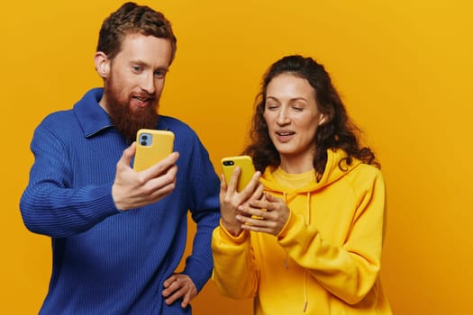 Man and woman couple smiling merrily with phone in hand social media viewing photos and videos, on yellow background, symbols signs and hand gestures, family freelancers. High quality photo