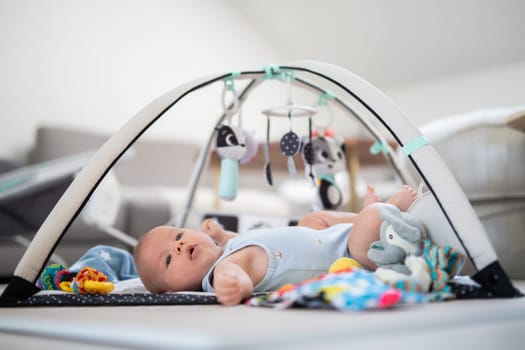 Cute baby boy playing with hanging toys arch on mat at home Baby activity and play center for early infant development. Baby playing at home.