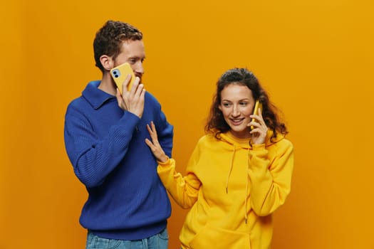 Woman and man cheerful couple with phones in hand talking on cell phone crooked smile cheerful, on yellow background. The concept of real family relationships, talking on the phone, work online. High quality photo