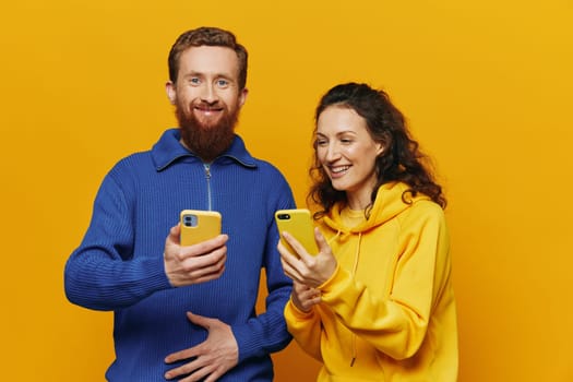 Man and woman couple smiling merrily with phone in hand social media viewing photos and videos, on yellow background, symbols signs and hand gestures, family freelancers. High quality photo