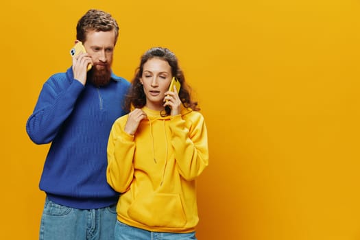 Man and woman couple smiling merrily with phone in hand social media viewing photos and videos, on yellow background, symbols signs and hand gestures, family freelancers. High quality photo