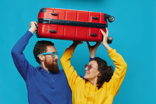 Woman and man smile suitcases in hand with yellow and red suitcase smile fun, on blue background, packing for a trip, family vacation trip. High quality photo