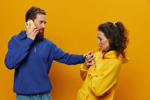 Woman and man cheerful couple with phones in hand social networking and communication crooked smile fun and fight, in yellow background. The concept of real family relationships, freelancers, work online. High quality photo